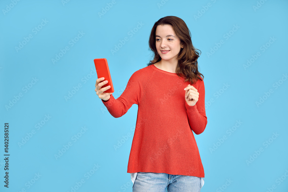Pretty smiling brunette girl in orange sweater looking at phone. Pretty smiling brunette girl in orange sweater looking at phone.