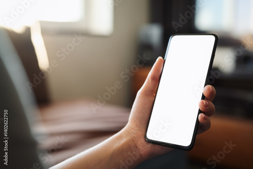 Young woman hold smartphone with white screen while sitting on a couch
