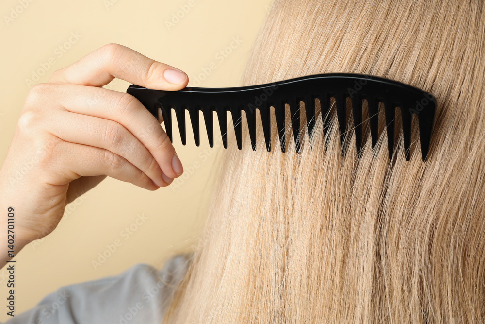 Obraz premium Woman brushing hair with plastic comb on beige background, closeup