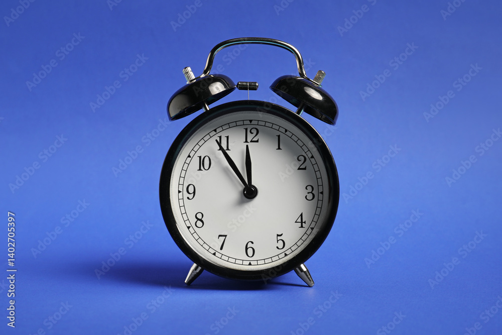 One black alarm clock on blue background One black alarm clock on blue background