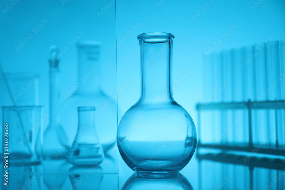 Laboratory glassware on mirror surface against light blue background Laboratory glassware on mirror surface against light blue background