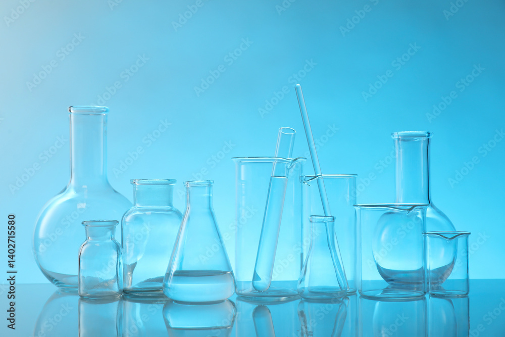 Laboratory glassware on mirror surface against light blue background Laboratory glassware on mirror surface against light blue background