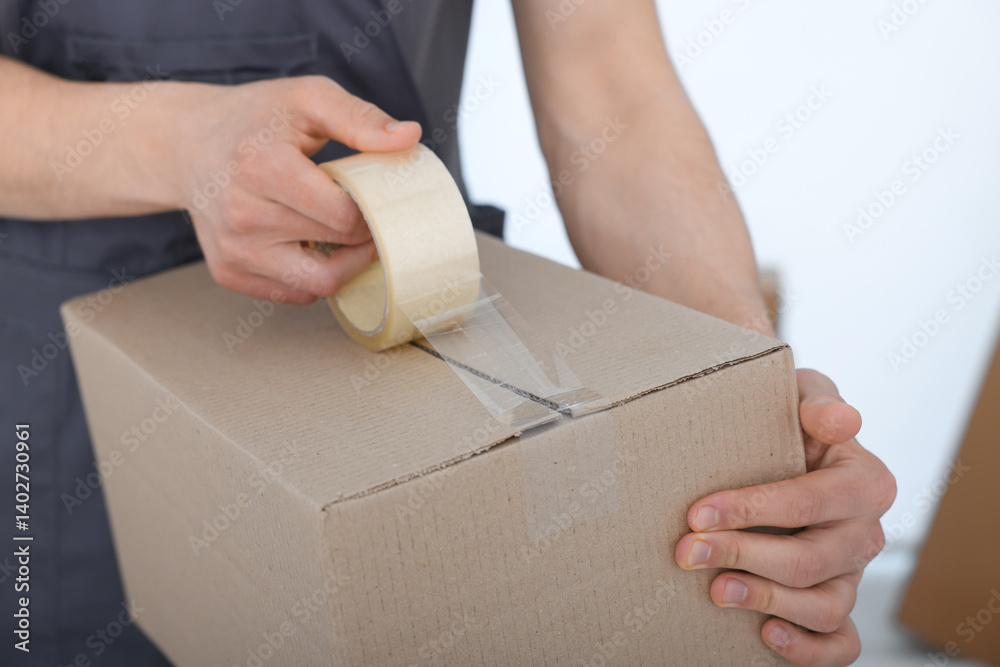 Man sealing cardboard box with adhesive tape indoors, closeup