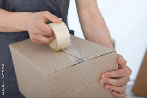 Obraz na płótnie Man sealing cardboard box with adhesive tape indoors, closeup w salonie