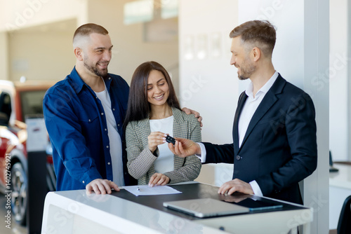 Quadro su tela Happy caucasian millennial couple receiving car keys from salesman after signing