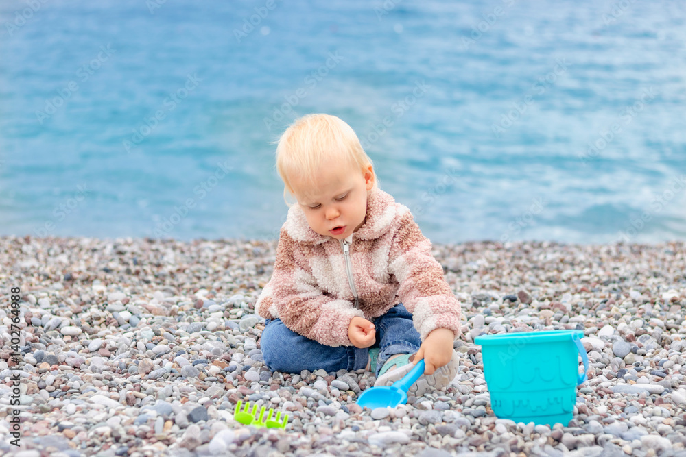 A young child happily explores a rocky beach, playing with colorful toys while enjoying the beautiful sea view