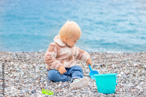A young child happily explores a rocky beach, playing with colorful toys while enjoying the beautiful sea view