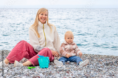 Obraz na płótnie A Loving Mother and Child Enjoying a Wonderful Beach Day on the Pebbly Shoreline w salonie