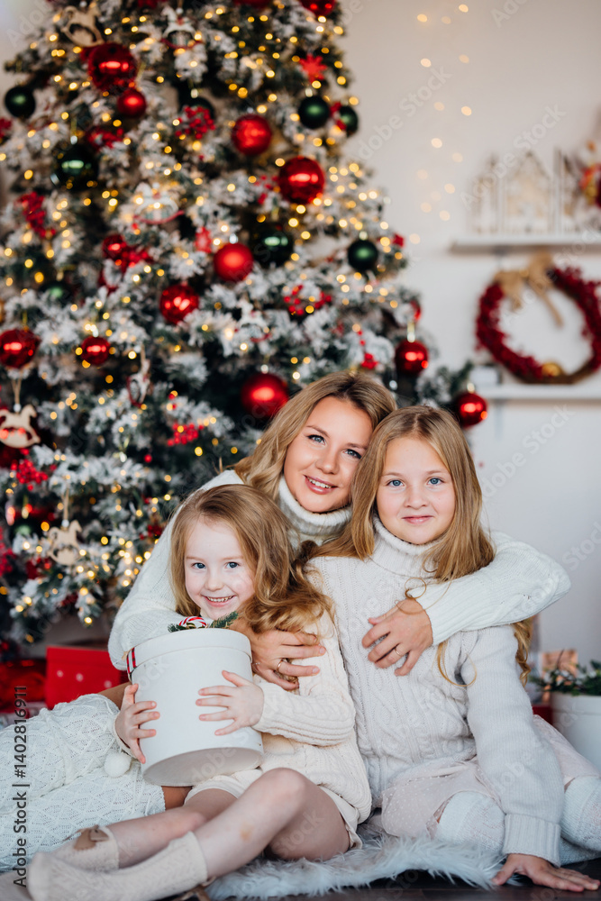 Mom and two cute daughters at the Christmas tree with gifts.