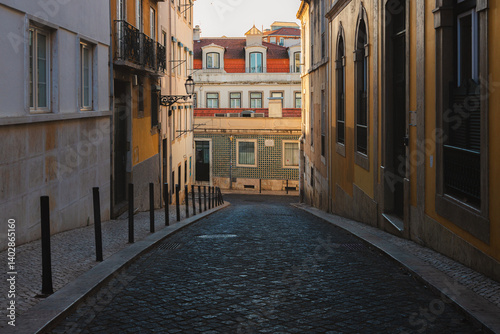 A narrow, cobblestone alley in Bairro Alto Lisbon, glows in the golden hour light, capturing the historic charm and serene atmosphere of this Portuguese old town on a quiet summer morning.