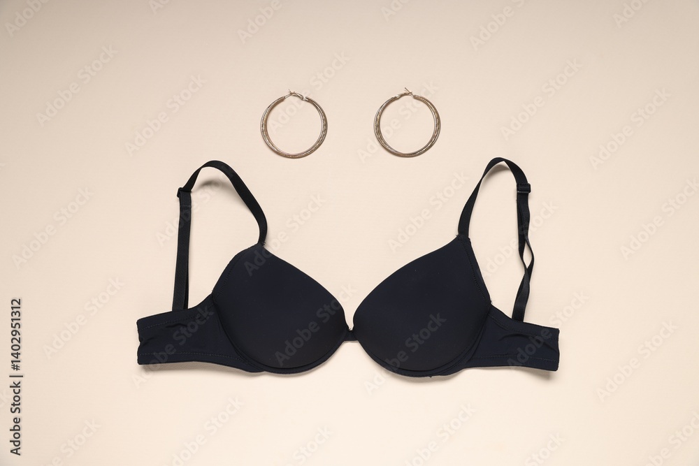 Black bra and earrings on beige background, flat lay Black bra and earrings on beige background, flat lay