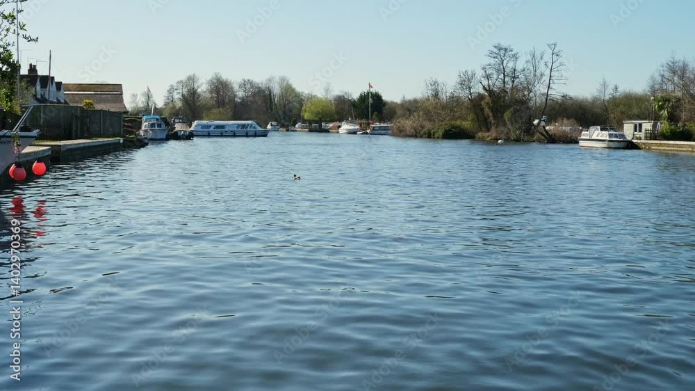View down the River Bure, Norfolk Broads. Captured from the riverbank in the small village of Horning on a bright and sunny morning. Static camera shot View down the River Bure, Norfolk Broads. Captured from the riverbank in the small village of Horning on a bright and sunny morning. Static camera shot