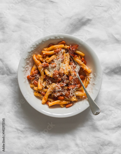 Quick and simple pasta with bacon and canned beans in tomato sauce on a light background, top view