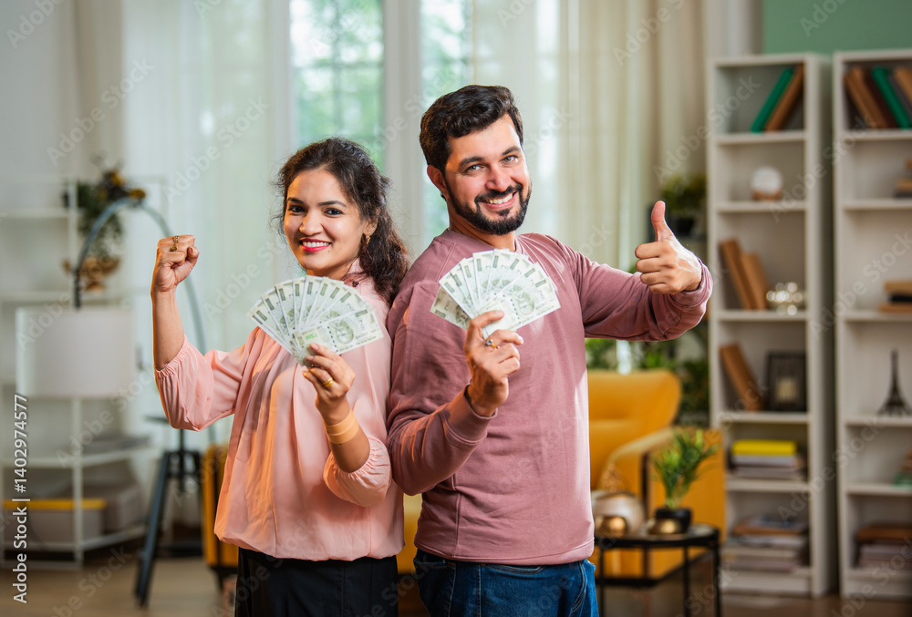 Obraz premium Joyful Indian couple holding rupee currency fan while standing in stylish home interior