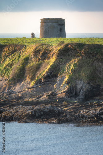 A breathtakingly picturesque view of a historic coastal Martello Tower, which stands majestically atop a towering cliff, surrounded by lush greenery and tranquil waters, Loughshinny, Dublin, Ireland
