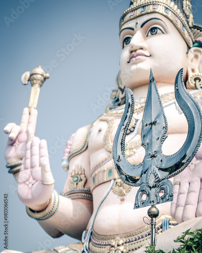 A powerful close-up of a grand Lord Shiva statue, highlighting the sacred trident (Trishula) in the foreground — a symbol of divine strength, protection, and cosmic balance in Hindu mythology.  photo