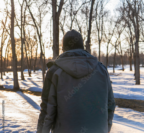 A solitary man dressed in a winter coat and beanie walks through a snow-covered forest at sunset. This peaceful winter scene captures the calm and introspective feeling of walking alone in nature 