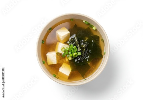 A bowl of miso soup with tofu, seaweed, and green onions on a white background from above view