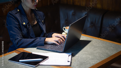 Confident businesswoman working on laptop on coffee shop table with tablet and paper, cafe manager managing store information
