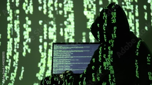 Zamaskowany cyberprzestępca w czarnym kapturze pracuje przy laptopie wśród zielonego kodu matrix – cyberatak, hakowanie systemu, dark web, haker w akcji, bezpieczeństwo cyfrowe, kodowanie danych