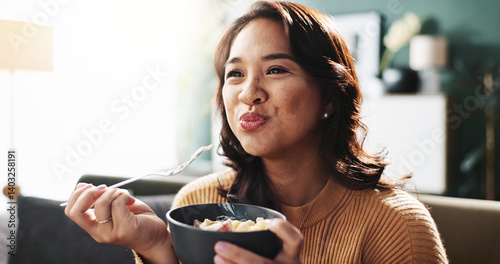 Happy, woman and eating food on sofa for dinner meal, nutrition and enjoyment with relax. Wellness snack, person and hungry with pasta bowl in living room for healthy diet, weekend break and cuisine photo