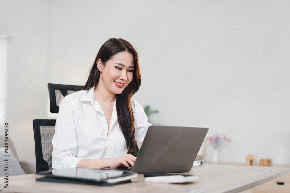 Asian businesswoman in white shirt works happily on laptop at modern office desk Asian businesswoman in white shirt works happily on laptop at modern office desk