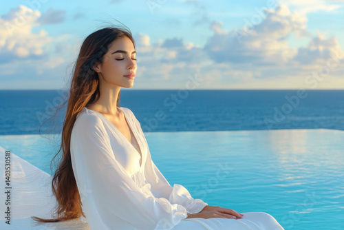 A serene woman in white enjoys a peaceful moment beside a calm infinity pool overlooking the ocean under a beautiful sky.