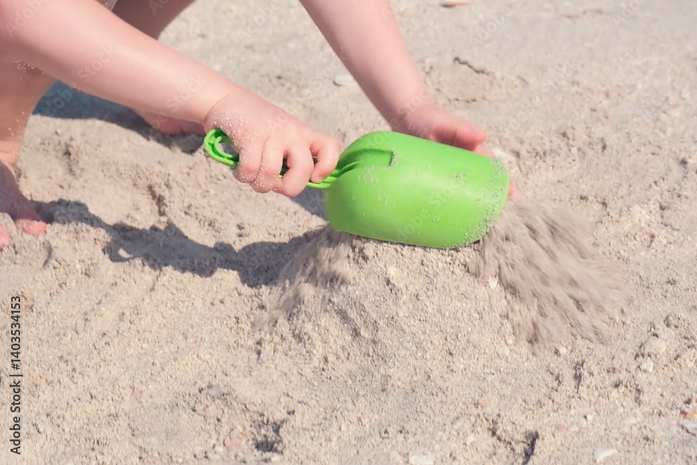 Hands of a child enthusiastically building sandcastle using a green toy shovel on a sandy beach. Depicts a playful and creative beach activity on a sunny day Hands of a child enthusiastically building sandcastle using a green toy shovel on a sandy beach. Depicts a playful and creative beach activity on a sunny day