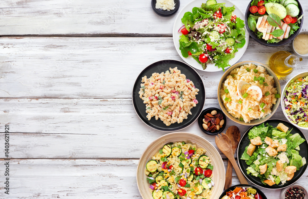 Variety of delicious homemade salads. Above view side border on a white wood background. Summer food concept. Potato, caesar, pasta and green salads.