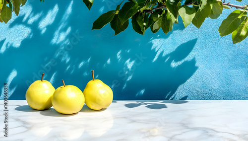Three Yellow Pears on White Marble Surface with Blue Textured Wall and Green Leaves Overhead in Bright Sunlight