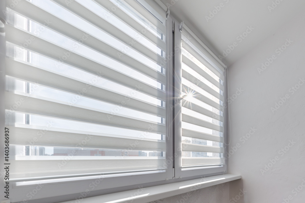 Modern double roller zebra blinds on large windows in bright minimalist interior with sunlight streaming through on balcony