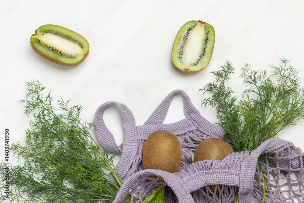 Two halves of kiwi fruit, avocado and bunches of dill in gray cotton mesh