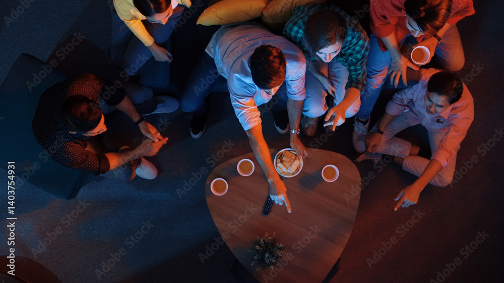 Diverse friend cheering football together while happy man holding snack bowl and remote at dark living room. Caucasian people watching movie and spending time together while eating snack. Convocation.