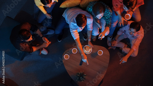 Obraz na płótnie Diverse friend cheering football together while happy man holding snack bowl and remote at dark living room. Caucasian people watching movie and spending time together while eating snack. Convocation. w salonie