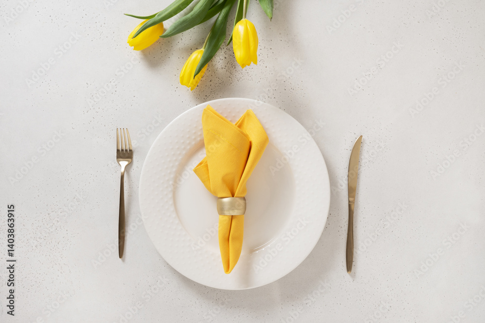 Spring table setting with yellow tulips, white plates and yellow napkin on white background. Happy Easter celebration. View from above.