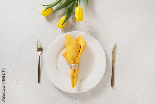 Obraz na płótnie Spring table setting with yellow tulips, white plates and yellow napkin on white background. Happy Easter celebration. View from above. w salonie