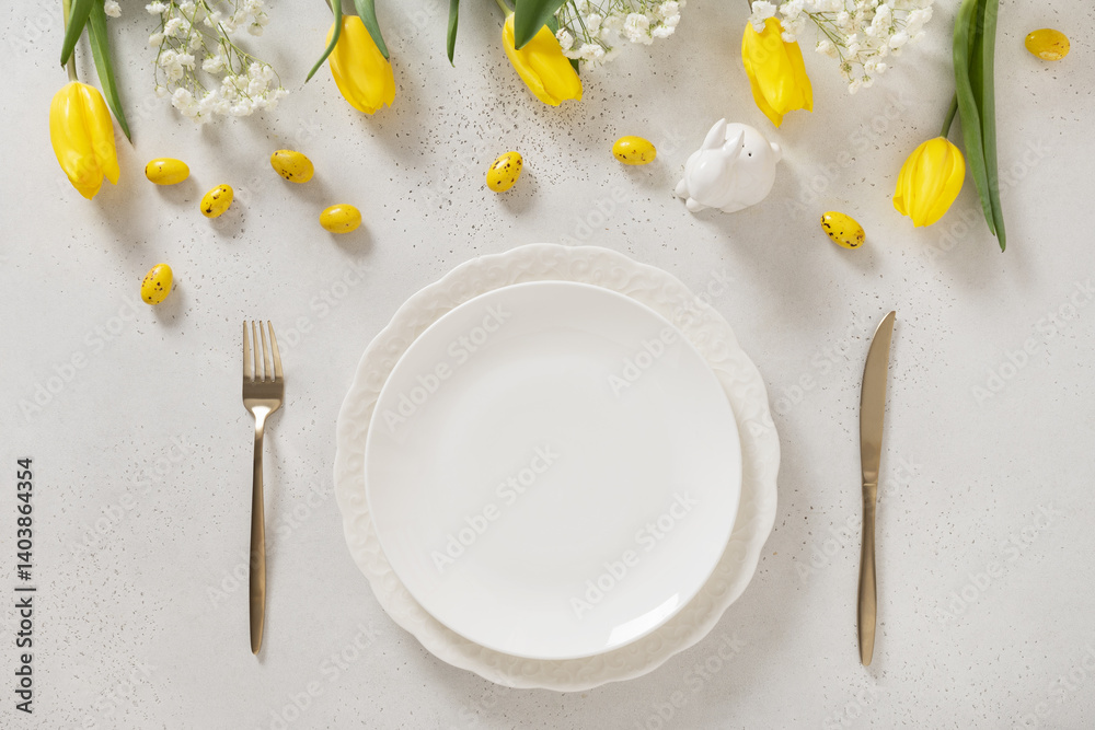 Easter table setting with spring, yellow tulips, white plates, bunny, eggs on white background. Happy Easter celebration. Copy space. View from above.