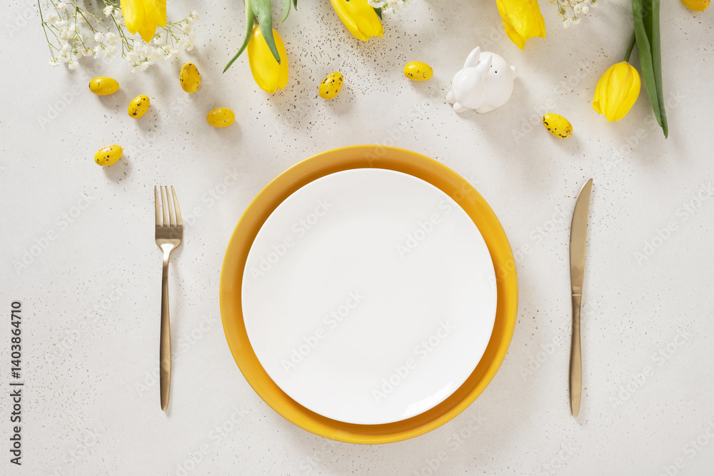 Easter table setting with spring yellow tulips, white plates, bunny, eggs on white background. Happy Easter celebration. Copy space. View from above.
