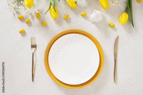 Obraz na płótnie Easter table setting with spring yellow tulips, white plates, bunny, eggs on white background. Happy Easter celebration. Copy space. View from above. w salonie