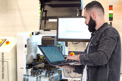 Technician programs and monitors automated manufacturing equipment using a laptop, working in the field of industrial automation and electronics production. photo