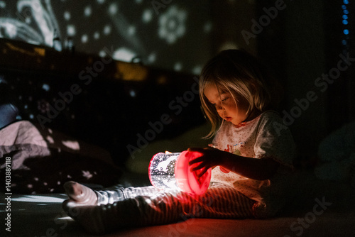 Little girl is looking at a night-light projector sitting on the bed