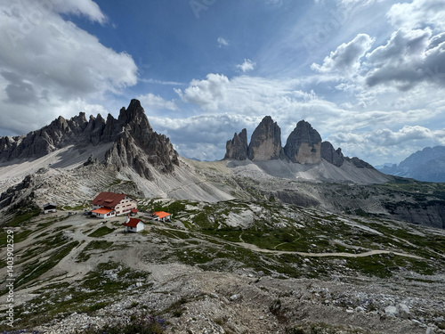 Famous mountain range Tre Cime di Lavaredo with surrounding peak monte paterno and mountain hut antonio locatelli in foredground at noon