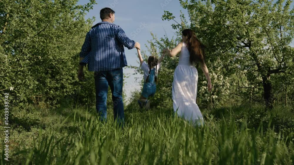 Kid girl plays with father mother. Happy family running in park holding hands in summer in park. Dad daughter Mom playing together in garden in spring, happy child holds parents hands, jumps. Teamwork Kid girl plays with father mother. Happy family running in park holding hands in summer in park. Dad daughter Mom playing together in garden in spring, happy child holds parents hands, jumps. Teamwork