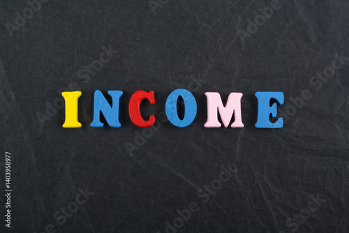INCOME word on black board background composed from colorful abc alphabet block wooden letters, copy space for ad text. Learning english concept. photo