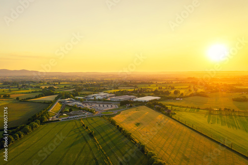 Aerial View of Rural Farmland and Industrial Buildings at Sunset – Golden Hour Countryside Landscape in Warm Evening Light