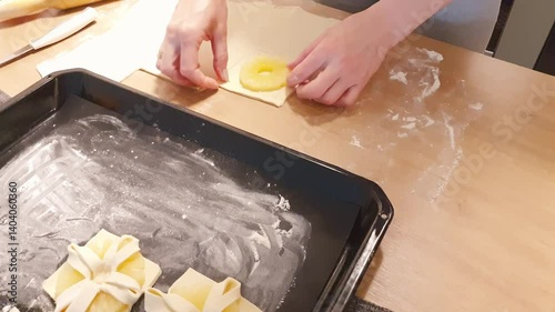 A woman wraps a pineapple wedge in puff pastry. Baking