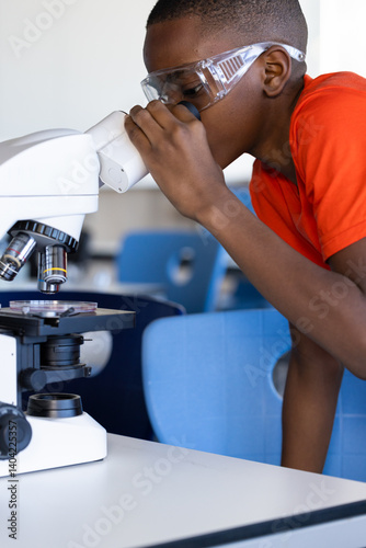 In school, boy using microscope and wearing safety goggles in science classroom