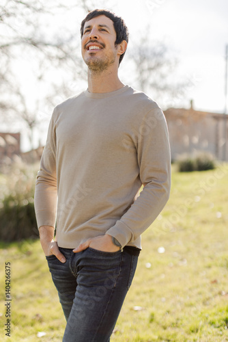 Portrait of a man with hands in pockets looking up and smiling in a sunny park. Transmits hope, gratitude, and presence, ideal for wellness, lifestyle, or personal growth projects. Vertical.