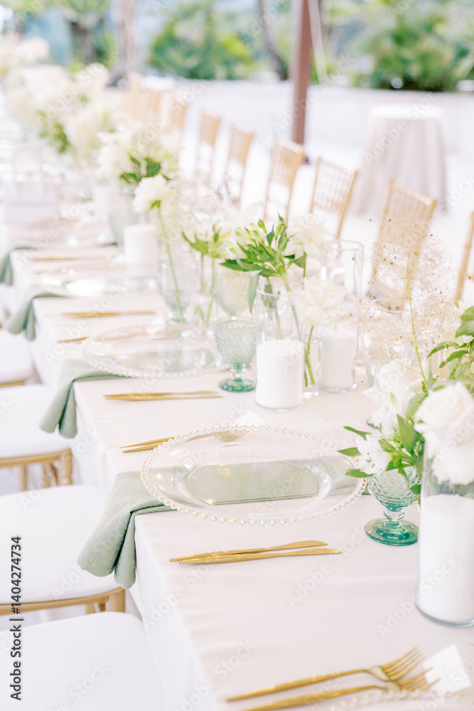 Long set festive table with bouquets of flowers, transparent crockery and candles Long set festive table with bouquets of flowers, transparent crockery and candles