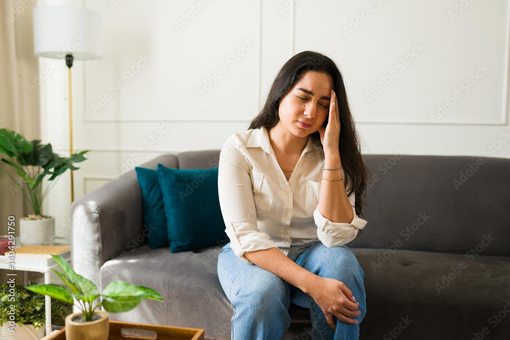 Distressed latina resting on couch, pressing forehead, experiencing intense migraine pain while dealing with overwhelming stress at home